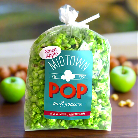 Bag of green apple popcorn with Midtown Pop label on a wooden surface with apples and popcorn.